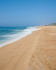 Fototapeta na wymiar Long sandy beach on a sunny day at Nazaré norte beach