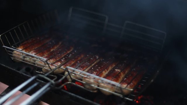 Cooking sausages in the grill. Smoking juicy meat sausages on the metal grate on the open barbecue. Street food concept.