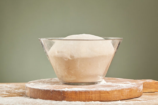 Dough in glass bowl on wooden cutting board. Close up.