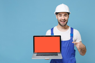 Excited man in coveralls hardhat point index finger on laptop computer with blank empty screen isolated on blue background. Instruments accessories for renovation apartment room. Repair home concept.