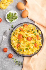 Reginelle semolina pasta with tomato, eggs and microgreen sprouts on a gray concrete background. Sde view, close up