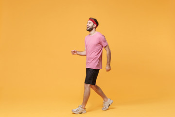 Fototapeta na wymiar Side view of cheerful young bearded fitness sporty guy sportsman in headband t-shirt spend weekend in home gym isolated on yellow background. Workout sport motivation lifestyle concept. Looking aside.