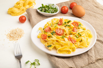 Reginelle semolina pasta with tomato, eggs, sesame and microgreen sprouts on a white wooden background. Side view, close up.