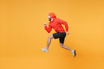 Fototapeta na wymiar Side view of young bearded fitness sporty guy 20s sportsman in hat hoodie, shorts in home gym isolated on yellow background in studio. Workout sport motivation lifestyle concept. Jumping like running.