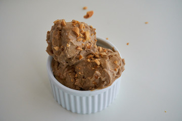Peanut butter banana ice cream scoops of ice-cream in a white bowl/cup with sprinkles of peanuts on top on a white table