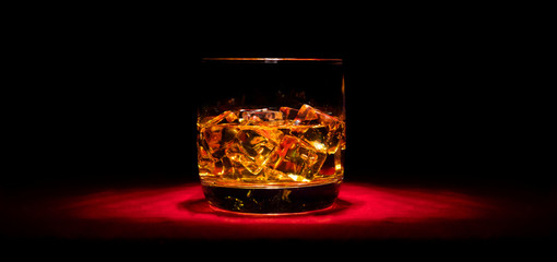 A glass of whiskey on the rocks on the red table in the middle