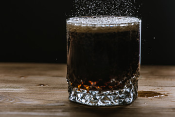glass with a drink of dark color side view, splashes and foam from the drink. Selective focus