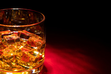 A glass of whiskey on the rocks on the red table. Side view