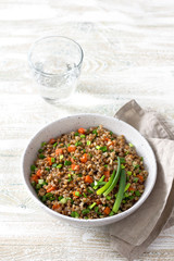 Delicious vegan buckwheat with vegetables and green onions on a light wooden background. Healthy homemade food