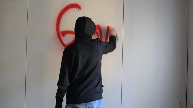 guy in a black sweatshirt inscribes spray paint on a clean wall in an abandoned building. View from the back