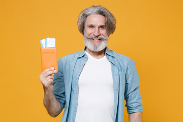 Smiling elderly gray-haired mustache bearded man in casual blue shirt posing isolated on yellow background in studio. People lifestyle concept. Mock up copy space. Hold passport tickets boarding pass.