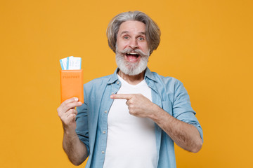 Excited elderly gray-haired mustache bearded man in casual blue shirt isolated on yellow background. People lifestyle concept. Mock up copy space. Point index finger on passport tickets boarding pass.