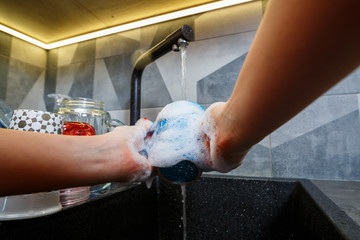 Hands with sponge wash the cup under water, housewife woman in washing blue mug in a kitchen sink...