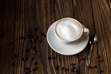 a Cup of coffee with milk and foam, coffee beans on a dark wooden background. selective focus