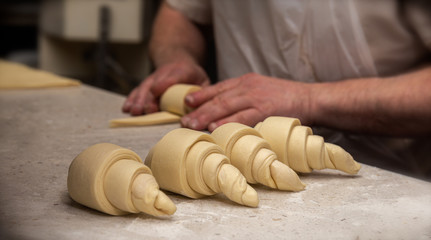 French baker rolling croissants on a granite bench top with flour on it