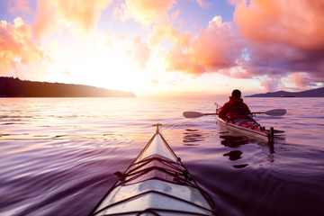 Adventurous Man Sea Kayaking in the Ocean during a colorful Sunset. Cloudy Sky Composite. Taken in...