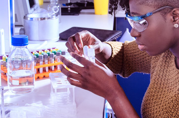 Young African female tech or scientist in protective glasses work with biological or medical liquid...