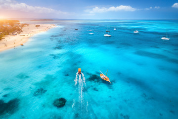 Aerial view of the yachts, fishing boats on tropical sea coast with sandy beach at sunset. Summer travel in Zanzibar, Africa. Landscape with boats in clear blue water, green palm trees. Top view
