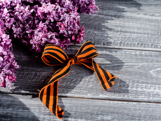 St. George's ribbon on a natural wooden background next to a branch of lilac, a symbol of Victory Day on may 9.