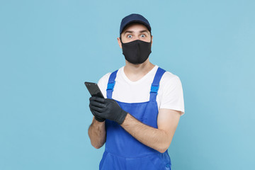 Delivery man in cap t-shirt uniform sterile mask gloves isolated on blue background studio. Guy employee courier hold mobile cell phone Service quarantine coronavirus virus covid-19 2019-ncov concept.