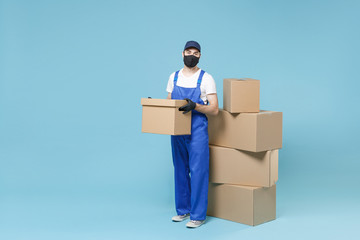 Full length delivery man in cap t-shirt uniform sterile face mask gloves isolated on blue background studio Guy employee courier hold box Service pandemic coronavirus virus covid-19 2019-ncov concept.