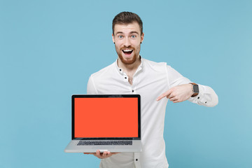 Amazed young bearded man guy 20s in white classic shirt isolated on blue background. People lifestyle concept. Mock up copy space. Pointing index finger on laptop pc computer with blank empty screen.