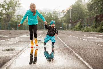 Boy and girl jumping in puddle in waterproof coat and rubber boots