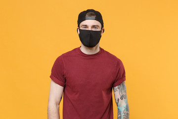Young tattooed man guy in casual t-shirt cap black face mask posing isolated on yellow wall...