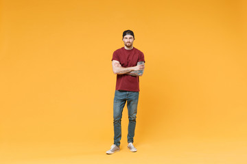 Attractive young tattooed man guy in casual t-shirt black cap posing isolated on yellow wall...