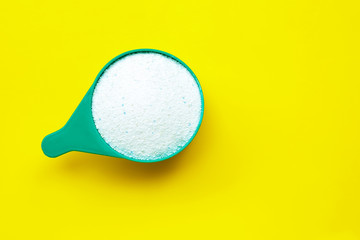 Measuring scoop with laundry powder on yellow background.