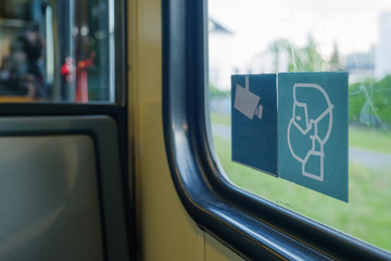 Fototapeta premium Selected focus at face mask covering mouth and nose symbol on blue sign on glass of public transportation's window door in Germany during epidemic of COVID-19 virus and German face mask regulations.
