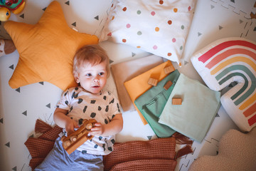 Happy baby boy playing with a wooden toy car lying on the floor