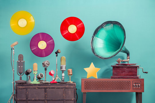 Antique gramophone phonograph turntable, old retro microphones, flying LP vinyl record discs, golden award star front mint blue background. Nostalgic music concept. Vintage style filtered photo