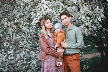 Beautiful young parents and their cute little son have fun near flowering trees