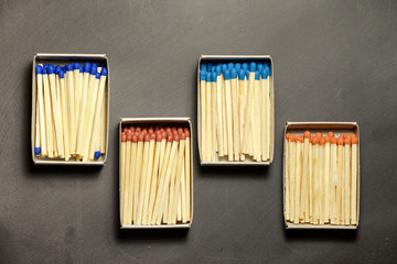 Matches of different colors in cardboard boxes on gray board. Boxes are staggered. The concept of achieving one goal by different departments of the enterprise.