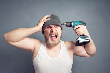 A guy with a creepy expression is holding a drill near his head. The concept of headache, abstract...