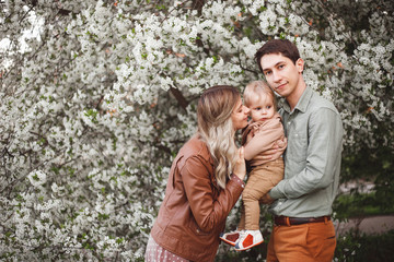Happy parents mom and dad, son stand in the garden in spring against the background of flowering trees