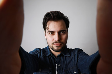Obraz premium Bearded man in the denim outfit which mixed with bright white t-shirt posing over white wall. Space for text.