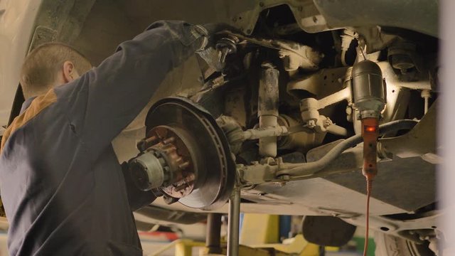 An Asian man is repairing the chassis of an old car lifted on a lift in a workshop, close-up.