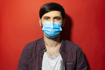 Studio portrait of young man wearing medical face mask against coronavirus on red background.