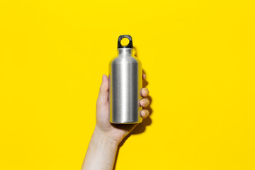 Close-up of male hand holding reusable aluminum thermo water bottle on background of yellow color.