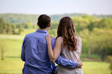 Handsome young couple with their arms around each other gazing out across a lush green park