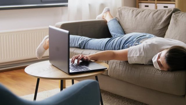 people, boredom and depression concept - sick bored young woman with laptop computer lying on sofa at home