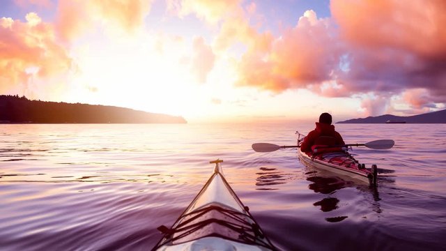 Adventurous Man Sea Kayaking in the Ocean during a colorful Sunset. Cloudy Sky Composite. Taken in Jericho, Vancouver, British Columbia, Canada. Cinemagraph Continuous Loop Animation.