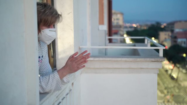 Coronavirus infection in Europe, worldwide flash mob in support of medical and police workers, quarantined middle-aged woman in mask applauding health workers. Stay at home isolation, fight against