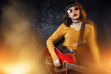 Hipster woman with curly hair play red guitar in neon lights. Rock musician is playing electrical...