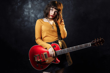 Hipster young woman with curly hair play red guitar in neon lights. Rock musician is playing...
