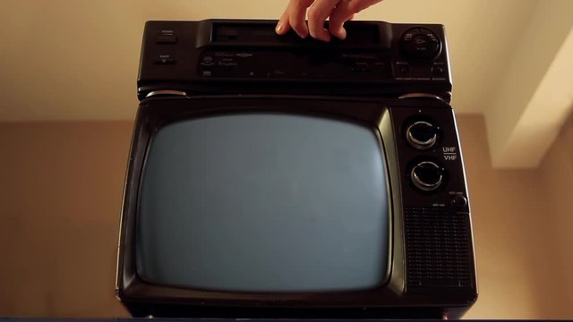Male Hand inserting a VHS into a VCR and an Old TV Green Screen. You can replace green screen with the footage or picture you want. You can do it with “Keying” effect in After Effects.