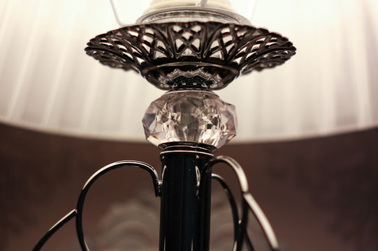 Close detailed picture  of a bedside silver lamp, which is decorated with a crystal and white lampshade