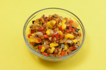 Cooked mango salsa with chopped red bell peppers and shallot onion in glass bowl on yellow background